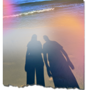 Shadow of two people standing on sandy beach with ocean waves gently crashing on the shore, symbolizing reflection and connection