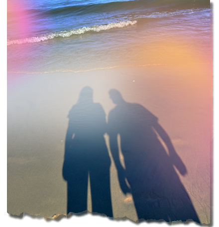 Shadow of two people standing on sandy beach with ocean waves gently crashing on the shore, symbolizing reflection and connection